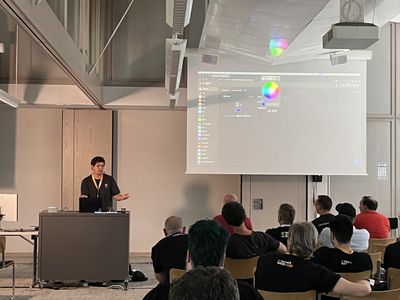 Speaker in front of the screen. On the screen, a TYPO3 backend with enabled color picker is shown. In front of the speaker, LED lights are shining.