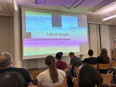 Photo of the audience looking to the canvas. The current slide is showing the words "Lots of Graphs" in the middle. Surrounded by multiple process diagrams.