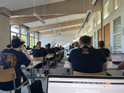 A room full of people, sitting in their place and waiting in front of their computers.